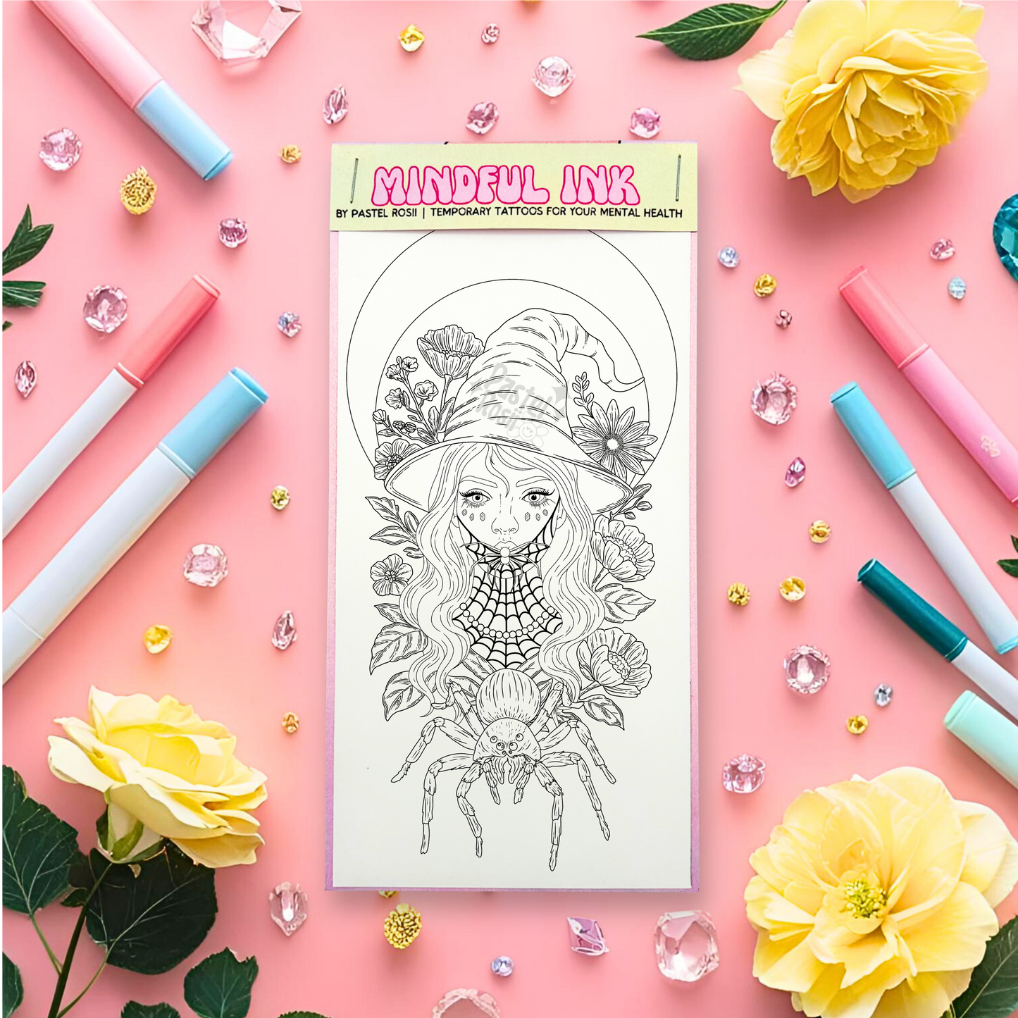 Temporary tattoo with floral and witch design on a pink background with markers and flowers.