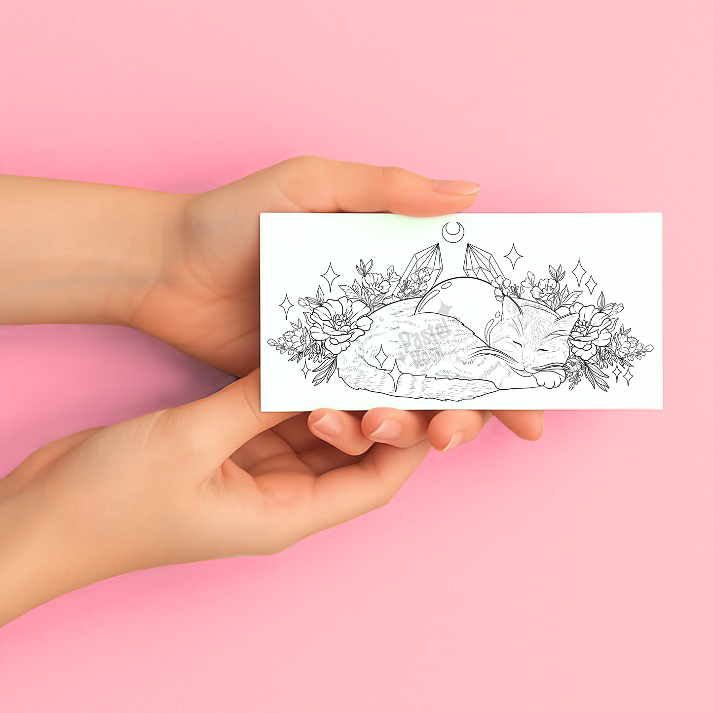 Hands holding a temporary tattoo with a black and white illustration of a cat, crystals, and flowers on a pink background.