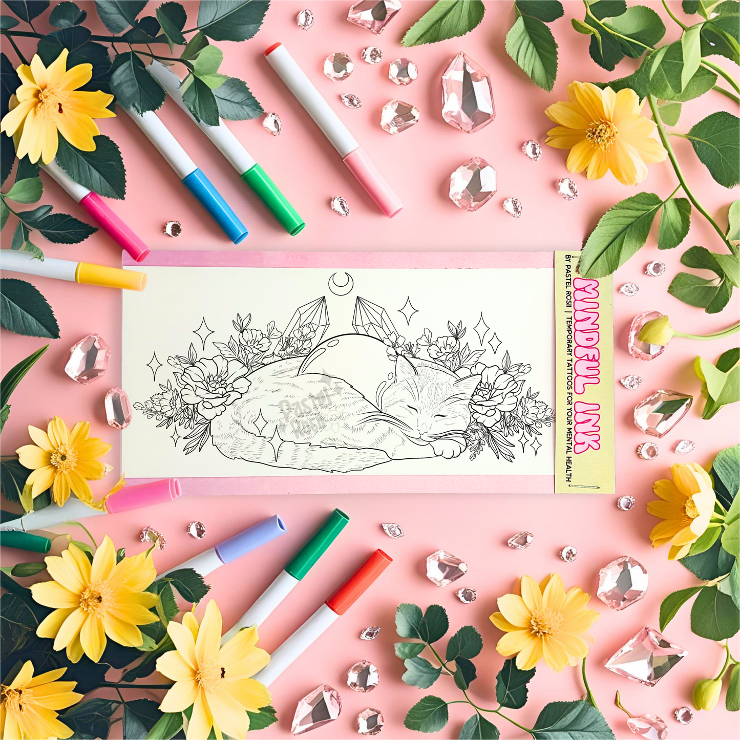 Temporary tattoo with a sleeping cat design, surrounded by markers, flowers, and crystals on a pink background.