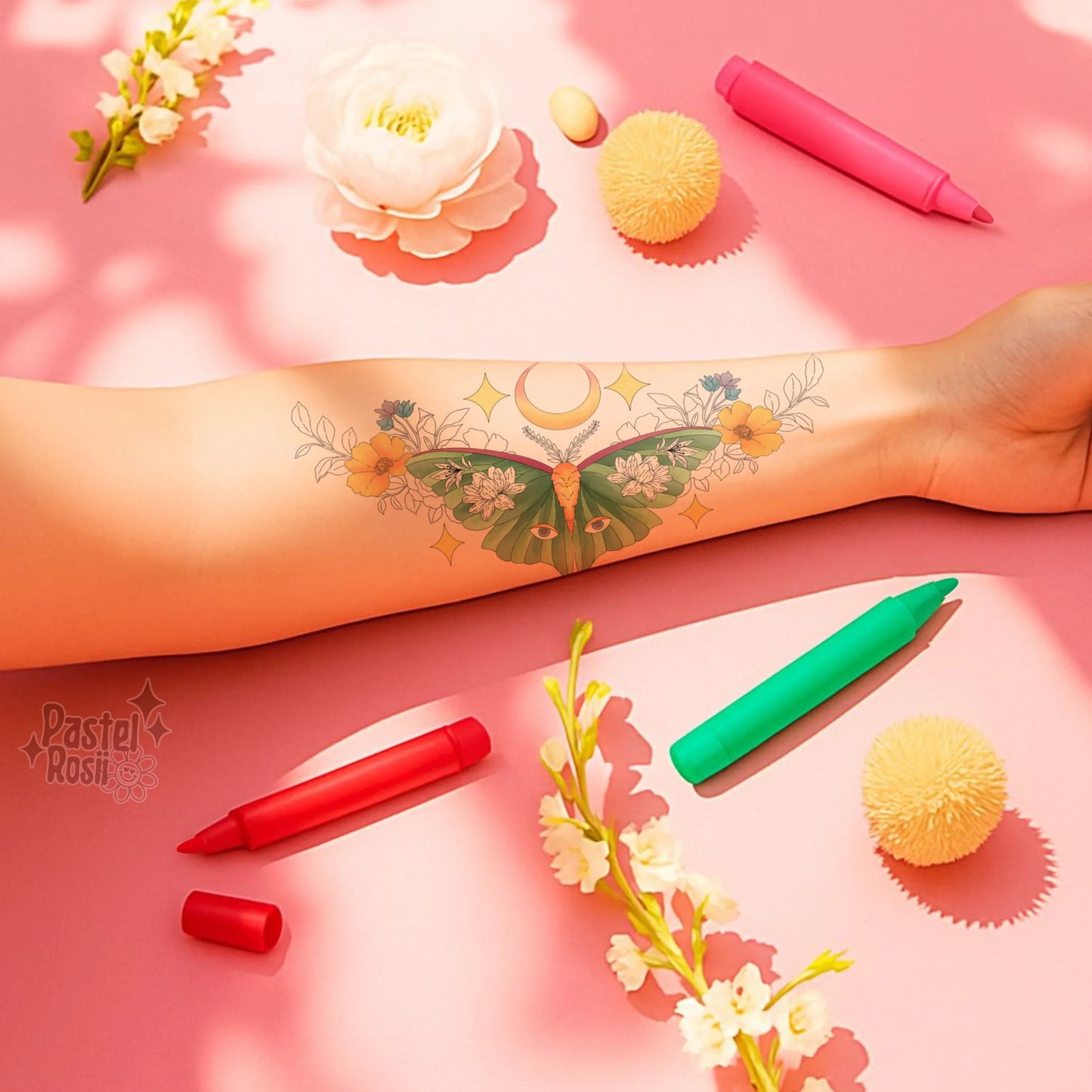 A vibrant arm tattoo of a butterfly surrounded by flowers and celestial elements, with colorful markers and decorative items on a pink background.