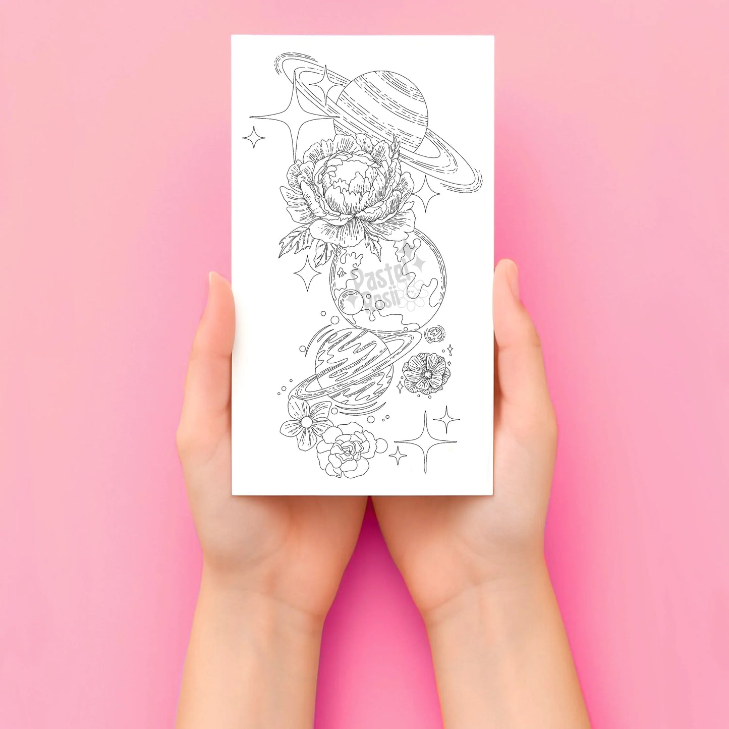 Hands holding a temporary tattoo with space-themed designs on a pink background