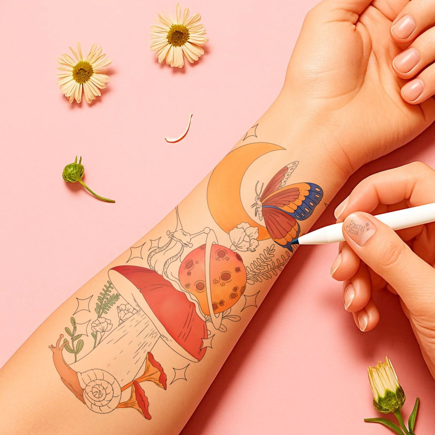 Hand with temporary tattoos of a butterfly, moon, and other designs on a pink background with flowers.