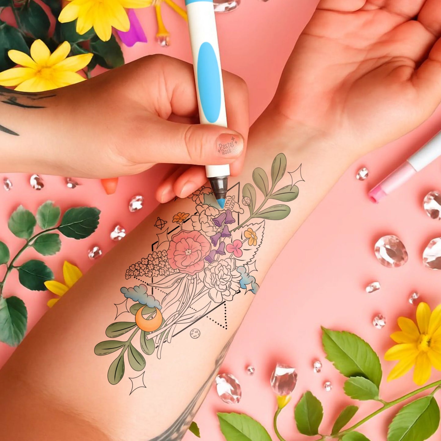 Hand applying temporary tattoo with floral design on arm against a pink background with flowers and rhinestones.