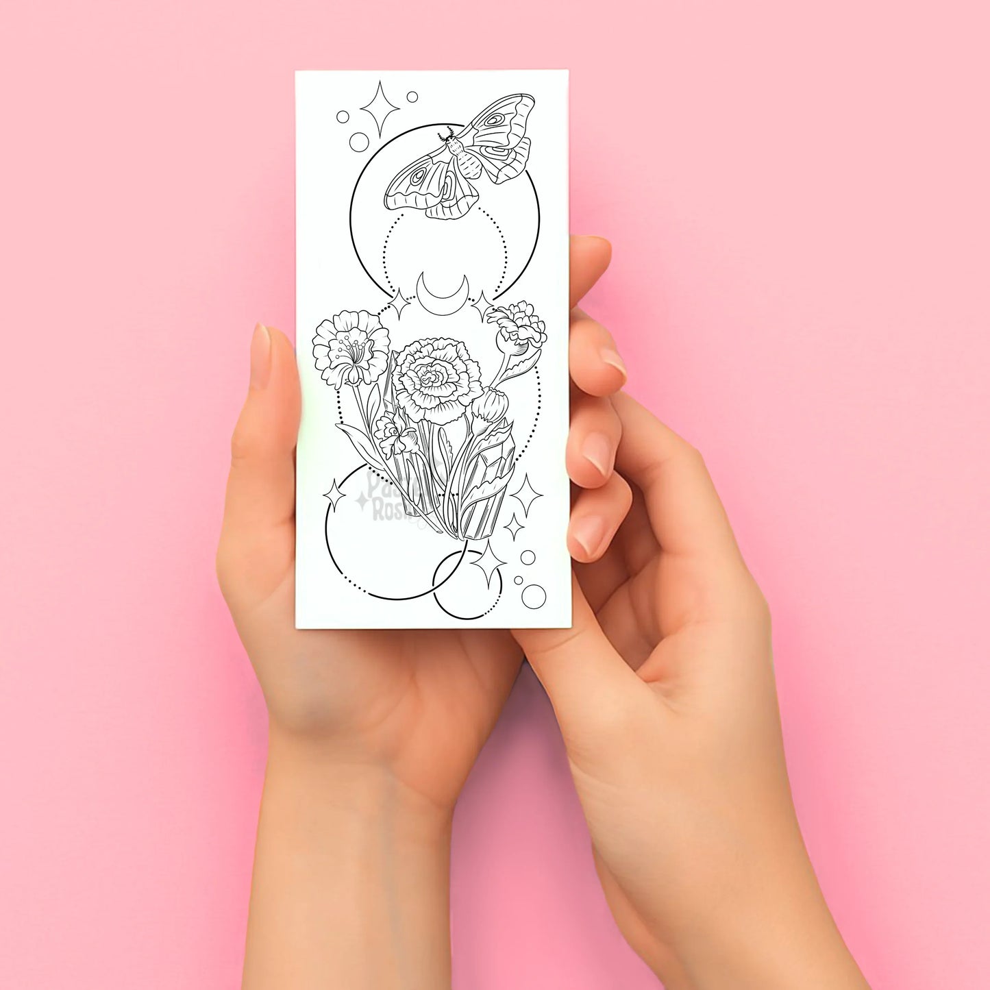 Hands holding a coloring tattoo page with floral and butterfly design on a pink background