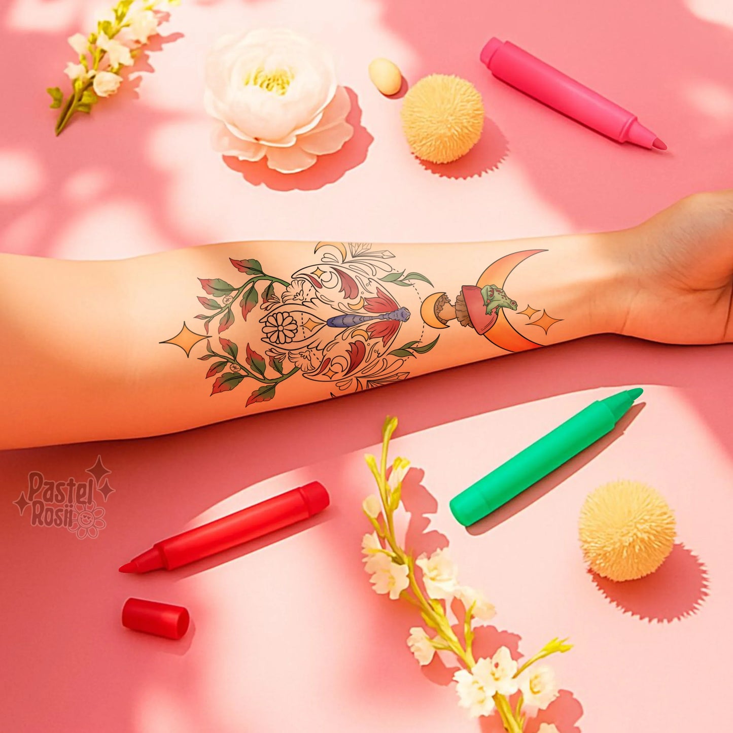 Tattoo of a colorful design on a person's arm with pastel-colored markers and flowers on a pink background.