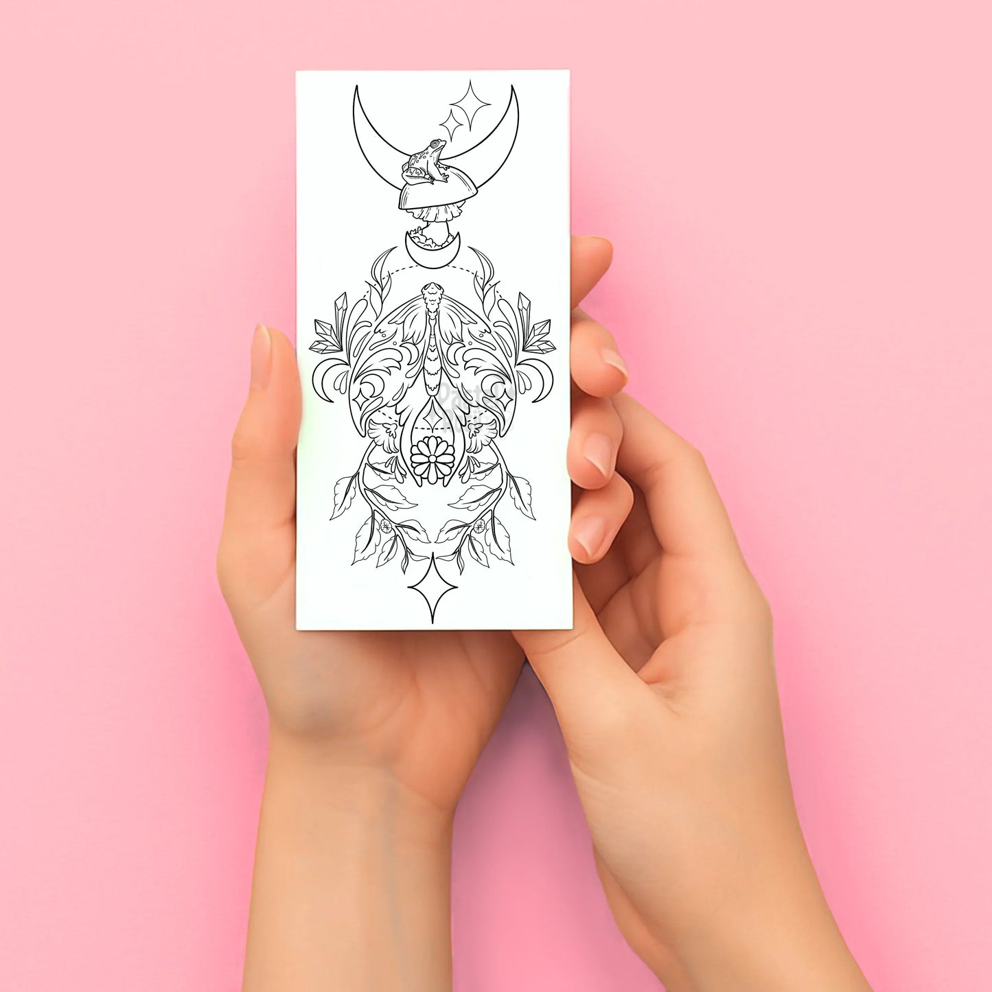 Hands holding a temporary tattoo with a black and white design against a pink background
