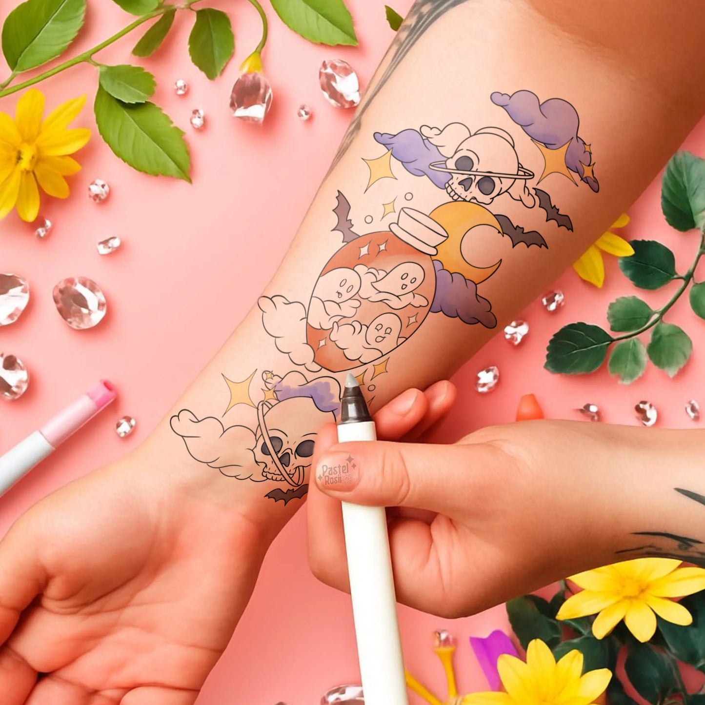 Temporary tattoo on a wrist with a colorful design, held by a hand against a pink background with flowers and leaves.