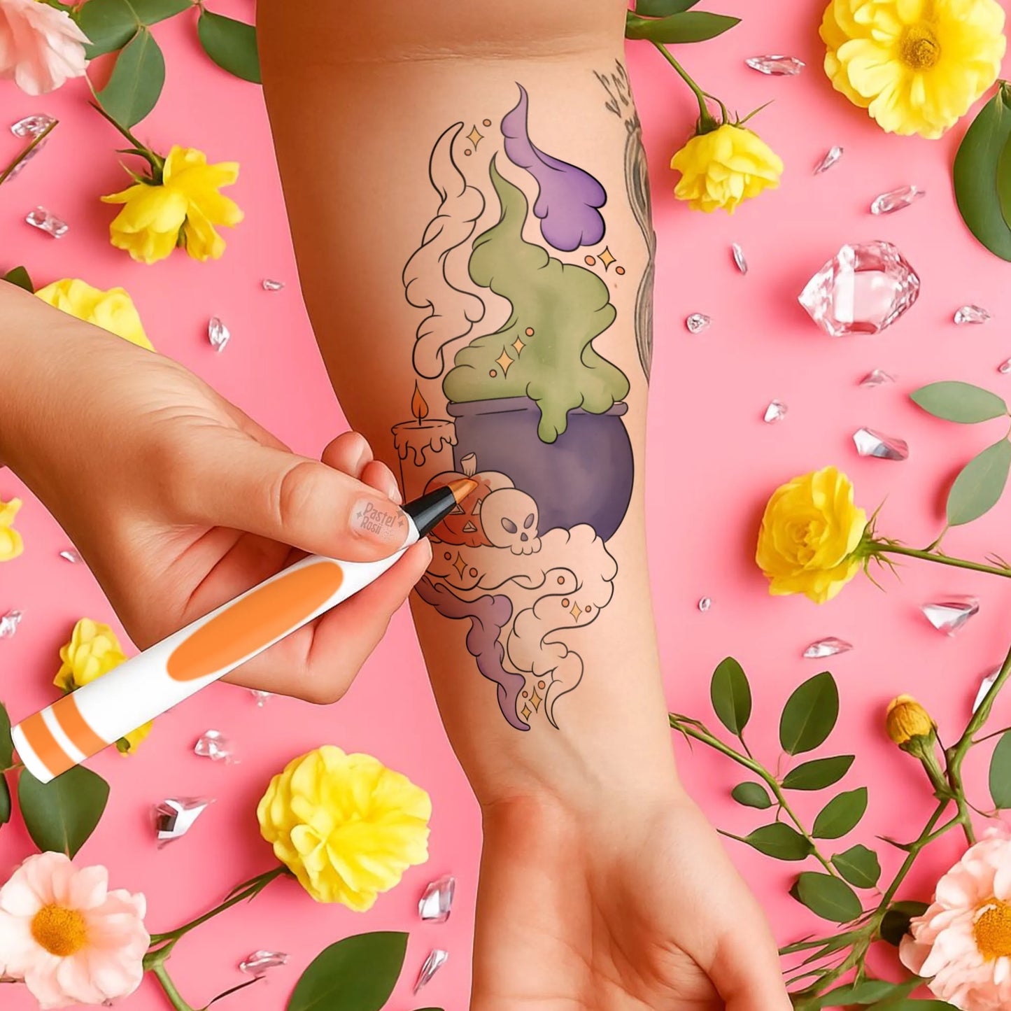 Person getting a tattoo of a colorful design on a pink background with flowers and crystals.