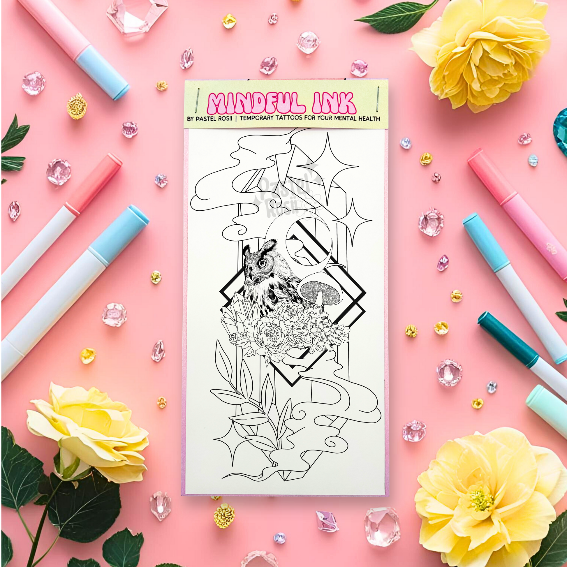 Temporary tattoo sheet with floral design surrounded by markers, flowers, and decorative items on a pink background