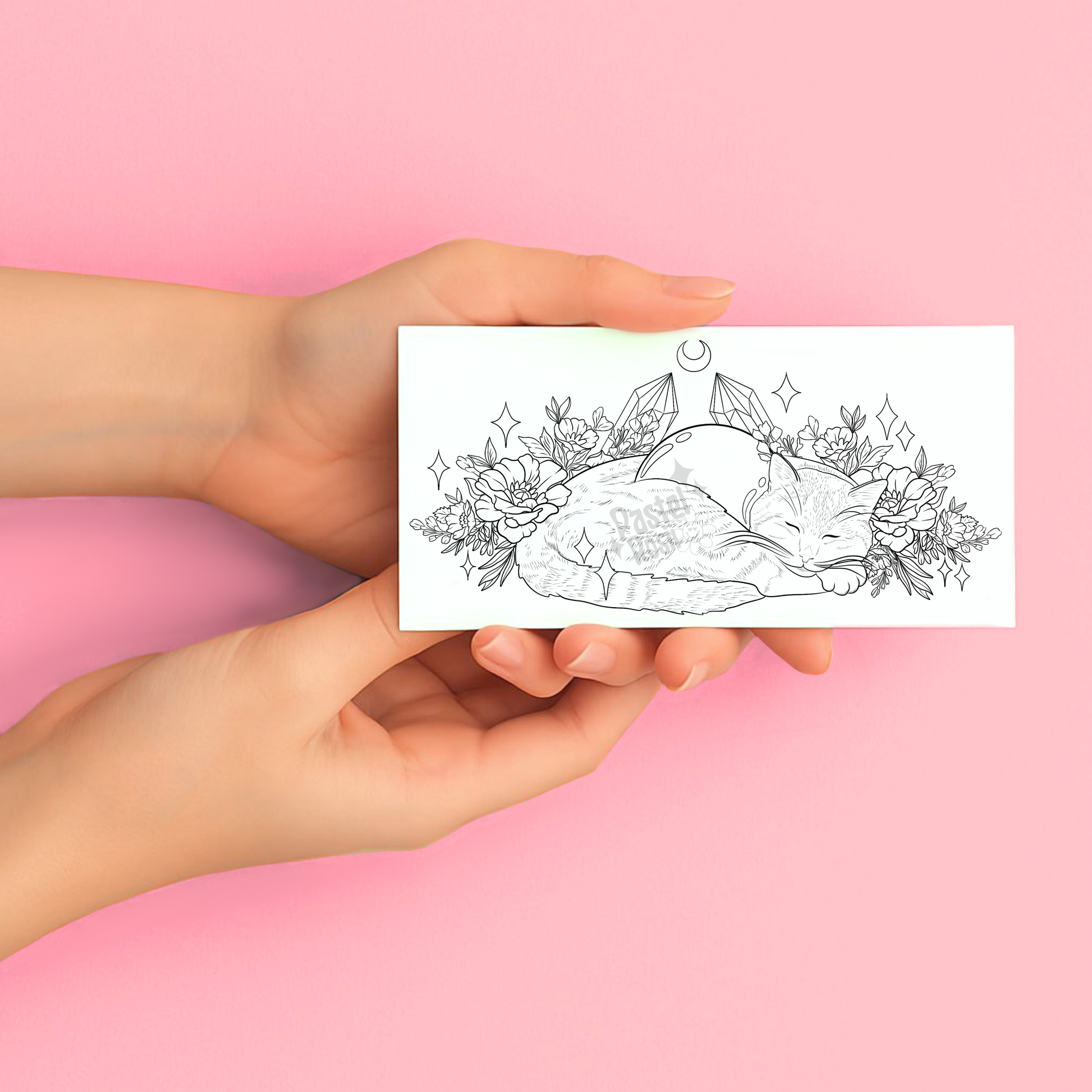 Hands holding a temporary tattoo with a black and white illustration of a cat, crystals, and flowers on a pink background.