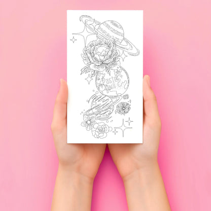 Hands holding a temporary tattoo with space-themed designs on a pink background