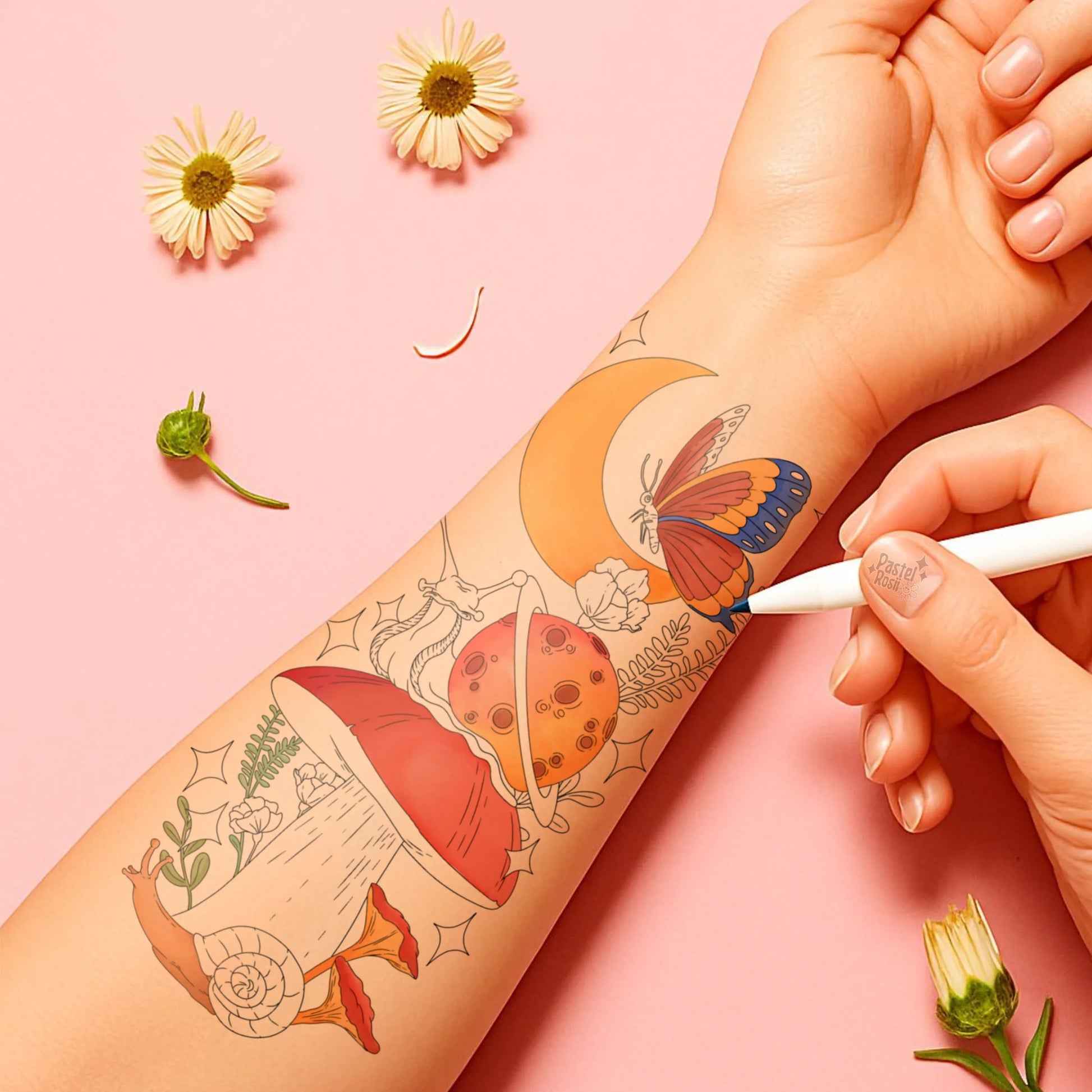 Hand with temporary tattoos of a butterfly, moon, and other designs on a pink background with flowers.