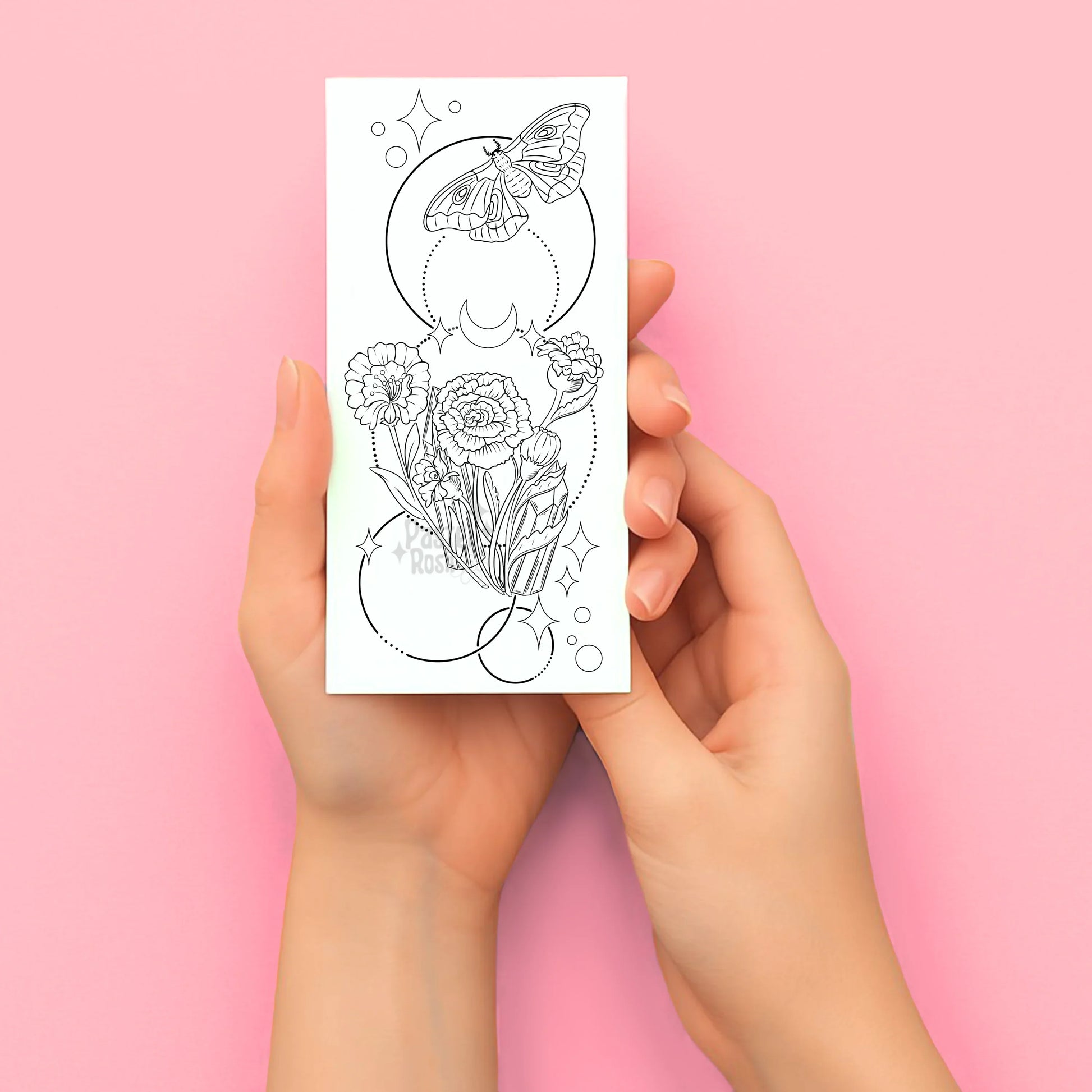 Hands holding a coloring tattoo page with floral and butterfly design on a pink background
