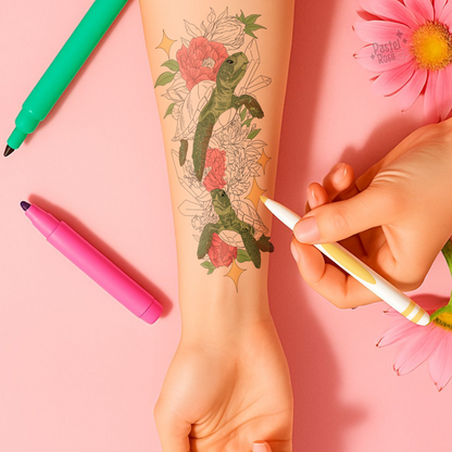 Tattoo of a turtle with flowers on a person's arm, with markers and flowers in the background.