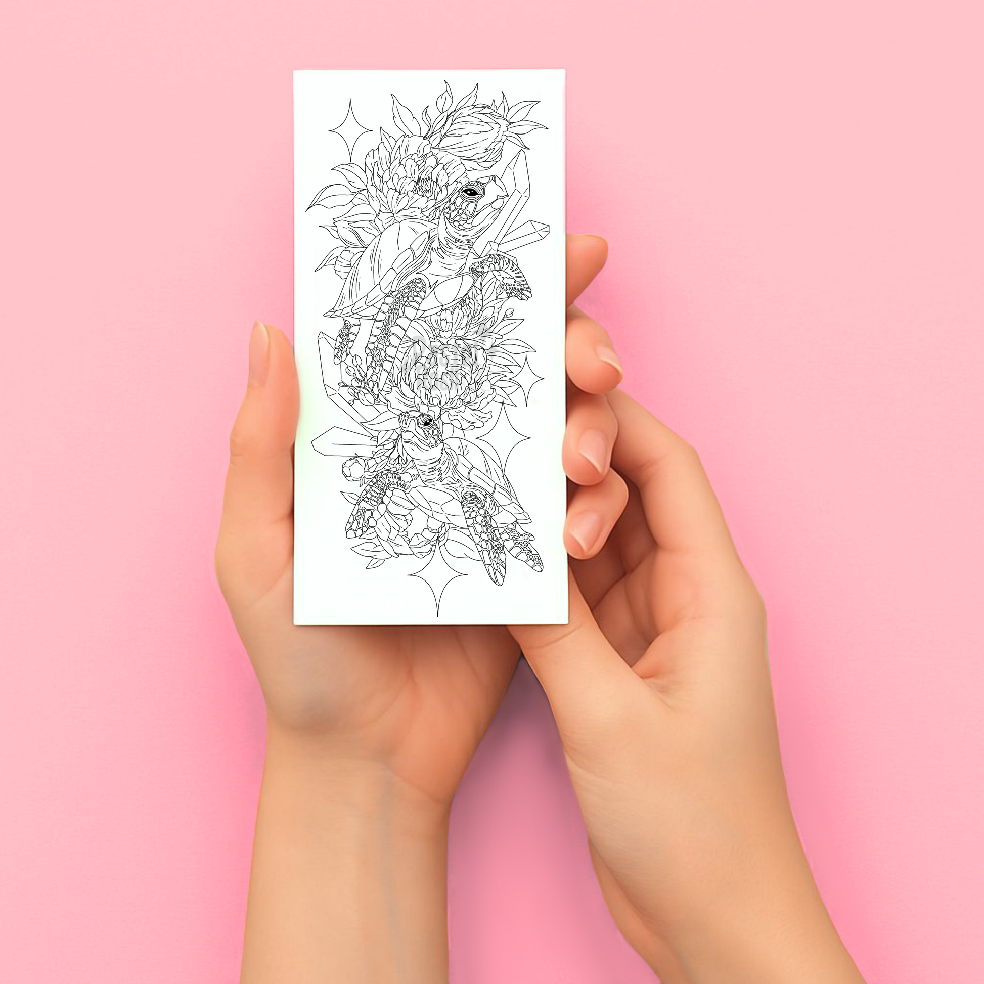 Hands holding a sheet of floral tattoo designs against a pink background