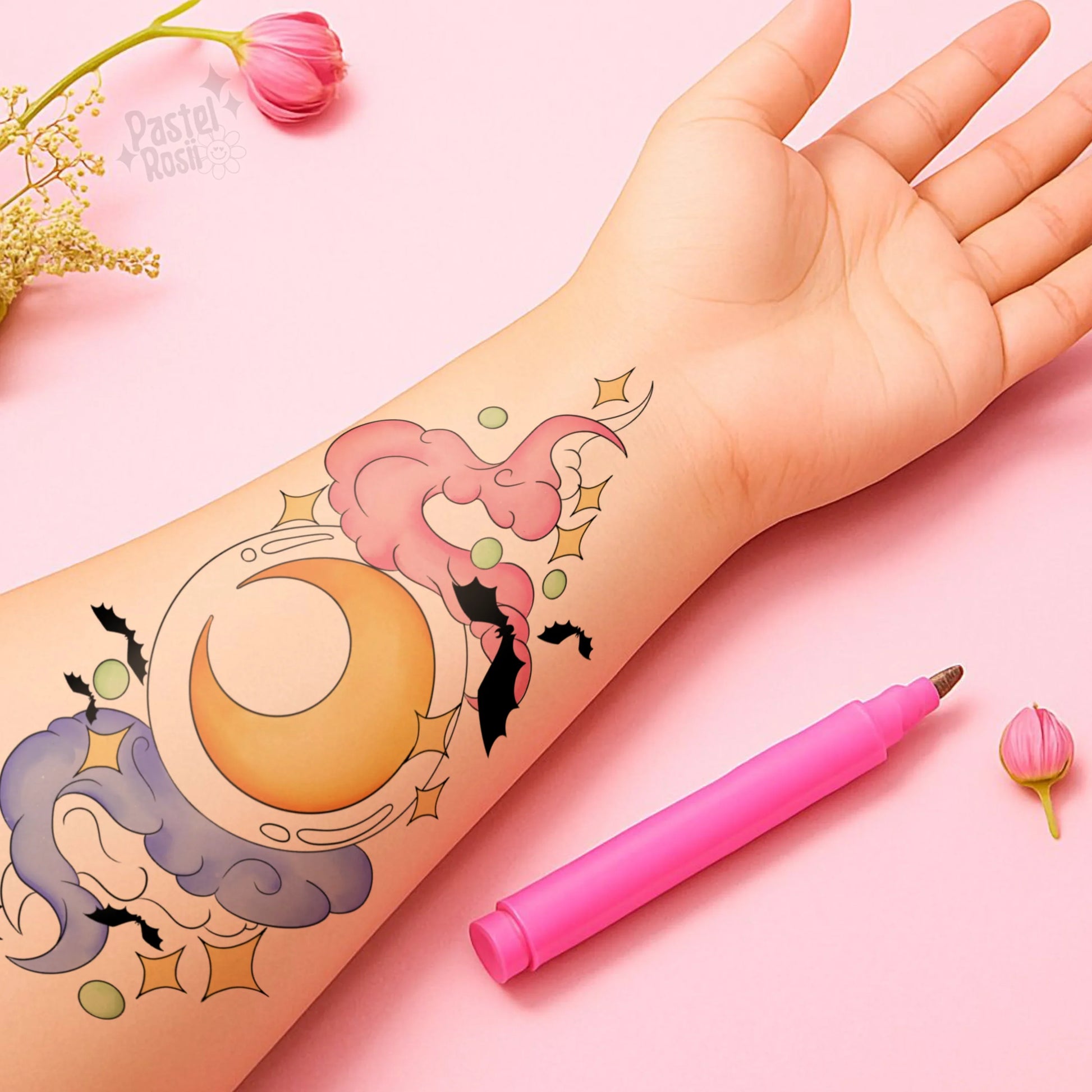 Hand with temporary tattoo of a moon and cloud design on a pink background with a pink pen.