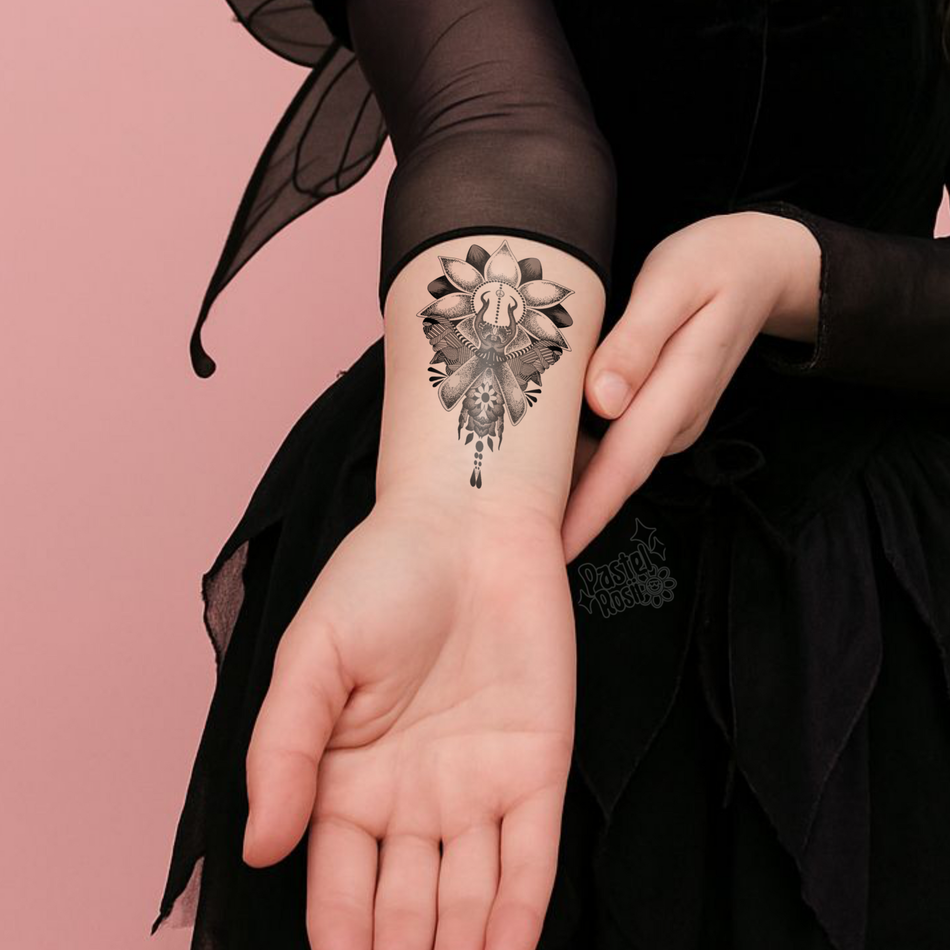 Person wearing a black sleeve with a detailed temporary tattoo on their wrist against a pink background